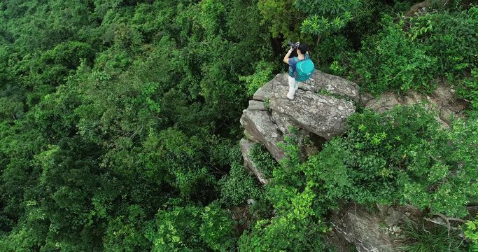 Aerial view of woman photographer taking pictures while hiking at tropical forest