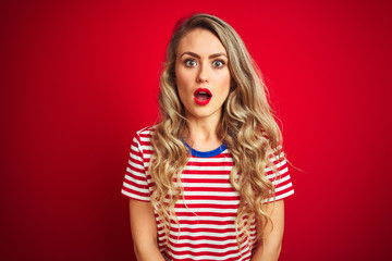 Young beautiful woman wearing stripes t-shirt standing over red isolated background afraid and shocked with surprise expression, fear and excited face.