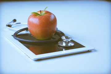 Medical stethoscope and red apple lying on a tablet isolated on white background.