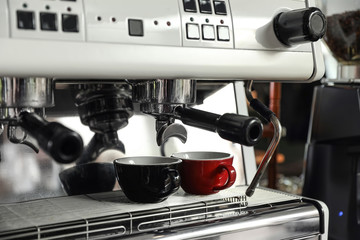 Modern coffee machine with cups in cafe, closeup