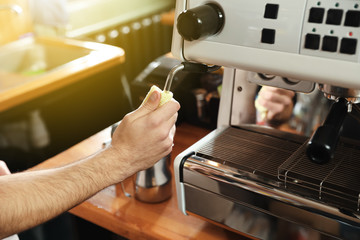 Barista cleaning coffee machine steam wand with rag on bar counter, closeup