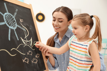 Kindergarten teacher and little child drawing on chalkboard indoors. Learning and playing