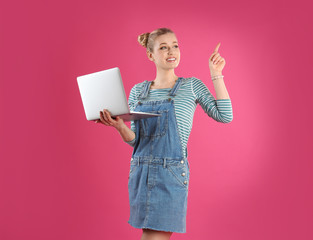 Portrait of young woman with laptop on pink background