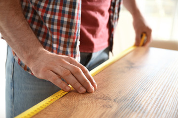 Man measuring wooden table, closeup. Construction tool