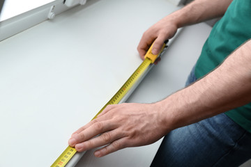 Man measuring white windowsill indoors, closeup. Construction tool