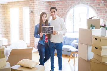 Fototapeta na wymiar Young beautiful asian couple smiling happy holding blackboard with new home text, hugging in love moving to a new house