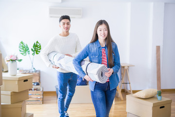 Beautiful young asian couple looking happy, holding rug smiling excited moving to a new home