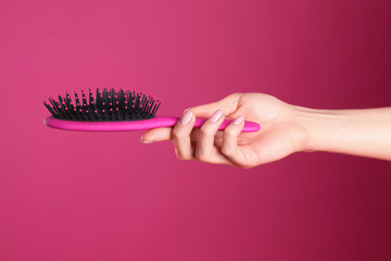 Woman holding hair brush against crimson background, closeup