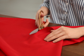 Woman cutting fabric with sharp scissors at wooden table, closeup. Space for text