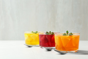 Glass bowls of natural jelly desserts on light table, space for text