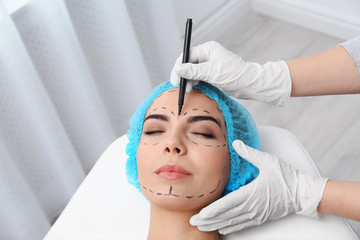 Doctor drawing marks on woman's face for cosmetic surgery operation in clinic