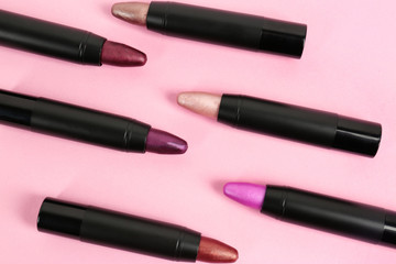 Set of bright lipsticks in black tubes on pink background, flat lay