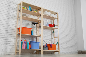 Wooden shelving units with cleaning equipment near white brick wall. Stylish room interior