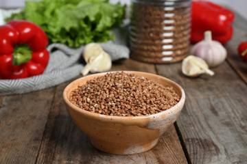 Ceramic bowl with uncooked buckwheat on wooden kitchen table