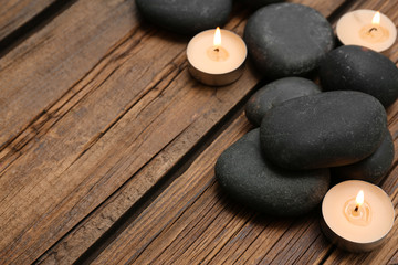 Fototapeta na wymiar Spa stones and lit candles on wooden background, space for text