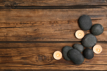 Spa stones and lit candles on wooden background, flat lay with space for text