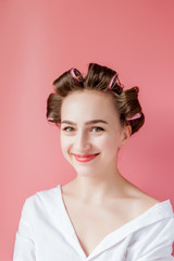 Beautiful girl in hair curlers on pink background