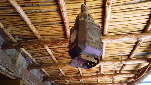 4K video of an old lantern hanging on a bamboo ceiling. The lantern is iron and rusty. It's a typical Berber style in Morocco.