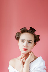 Beautiful young girl with a mask and curlers touching her face.