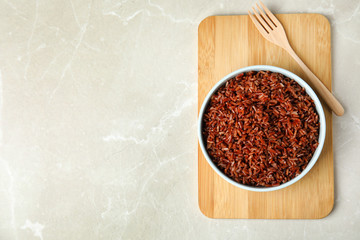 Bowl with delicious cooked brown rice on white marble table, top view. Space for text