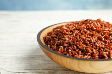 Bowl with delicious cooked brown rice on white wooden table, closeup. Space for text
