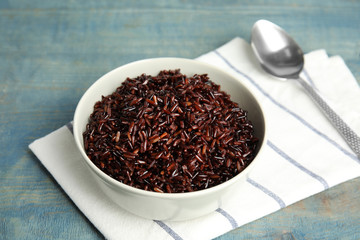 Bowl with delicious cooked brown rice on color wooden table