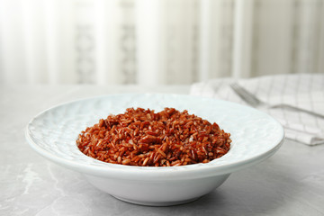 Plate with delicious cooked brown rice on grey table