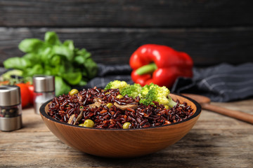 Bowl with delicious cooked brown rice on wooden table