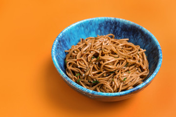 Bowl of buckwheat noodles on color background