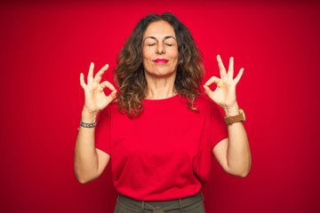 Middle age senior woman with curly hair over red isolated background relax and smiling with eyes closed doing meditation gesture with fingers. Yoga concept.