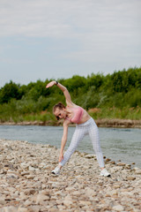 Girl in sports uniforms makes a stretch on the river bank