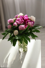Vase with bouquet of beautiful peonies on table in room