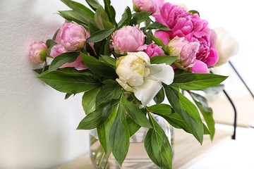 Shelf with vase of beautiful peonies on white wall