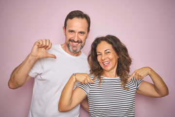 Beautiful middle age couple together standing over isolated pink background looking confident with...