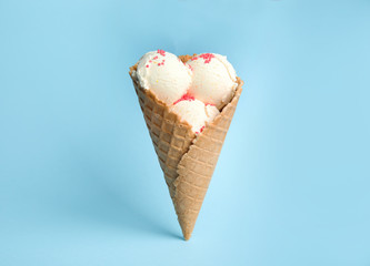 Delicious vanilla ice cream in wafer cone on blue background