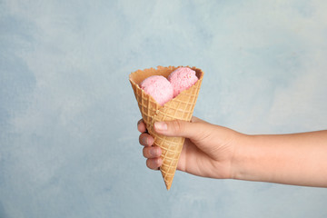 Woman holding delicious ice cream in wafer cone on light blue background, closeup