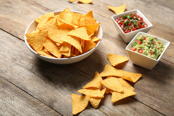 Bowl of delicious mexican nachos chips and sauces on wooden table