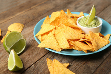 Plate with delicious mexican nachos chips, guacamole sauce and lime on wooden table
