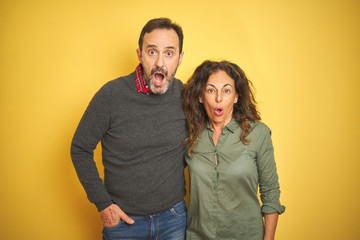 Obraz premium Beautiful middle age couple over isolated yellow background afraid and shocked with surprise expression, fear and excited face.