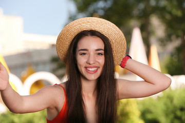 Happy young woman in stylish hat taking selfie outdoors on sunny day
