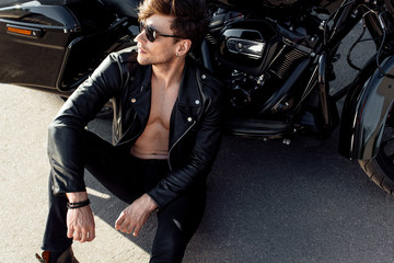 Obraz na płótnie Canvas shirtless young man sitting on ground near black motorcycle