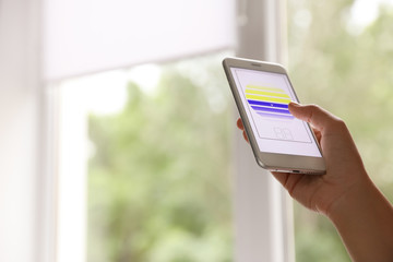 Woman using smart home application on phone to control window blinds indoors, closeup. Space for text