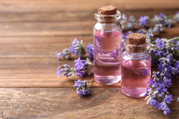 Obraz na płótnie Canvas Bottles with natural lavender oil and flowers on wooden table, closeup view. Space for text