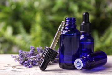 Bottles with natural lavender essential oil on white wooden table against blurred background. Space...