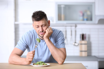 Portrait of unhappy man eating broccoli salad in kitchen