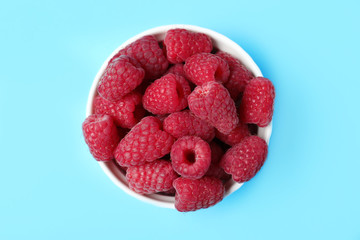 Bowl of delicious ripe raspberries on blue background, top view