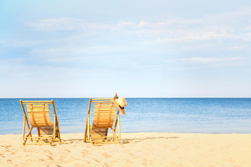 Fototapeta na wymiar Empty wooden sunbeds with hat on sandy shore. Beach accessories