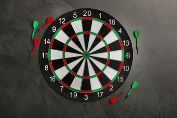 Dart board with color arrows on grey stone background, top view