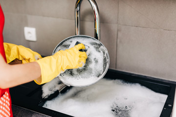 Close up of woman hand in yellow protective rubber gloves washing dishes in the kitchen. - Powered by Adobe