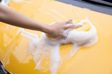 Close-up Of Hand With sponge Washing yellow Car